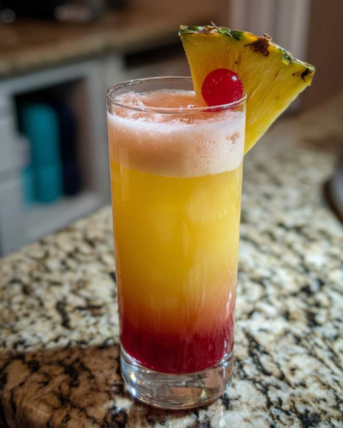 A layered Piña Colada Sunrise Mocktail showing yellow, orange, and red layers, garnished with a pineapple wedge and cherry.