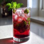 A tall glass filled with a vibrant red Pomegranate Spritz with Fresh Mint, ice, and bubbles.