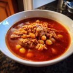 Close-up of a white bowl filled with rich, red Pozole Rojo with Pork and Hominy.
