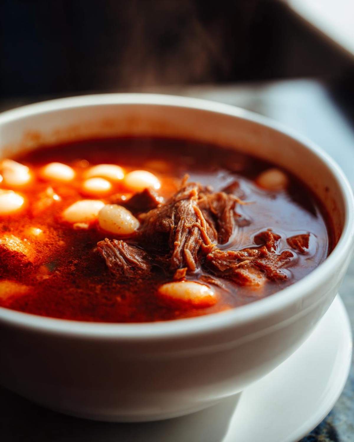 Close-up of a steaming white bowl filled with rich red Pozole Rojo with Pork and Hominy.