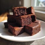 A stack of rich, dark chocolate Protein Brownie Bites with Collagen cut into squares, resting on a white plate.