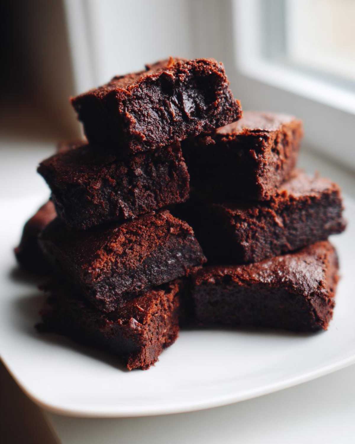 A stack of rich, dark chocolate Protein Brownie Bites with Collagen, showing a fudgy interior texture.