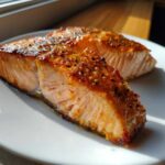 Close-up of two perfectly cooked, flaky Ridiculously Good Air Fryer Salmon fillets with a caramelized, seasoned crust on a white plate.