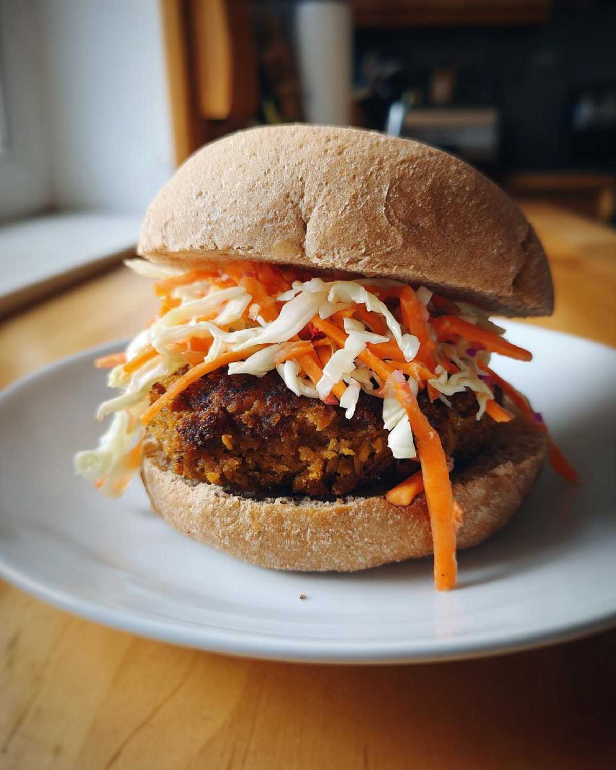 A close-up of a Roasted Cabbage Burger patty served on a whole wheat bun topped generously with shredded carrots and cabbage slaw.