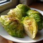 Four wedges of Roasted Cabbage with Garlic Butter seasoned with pepper, served on a white plate.