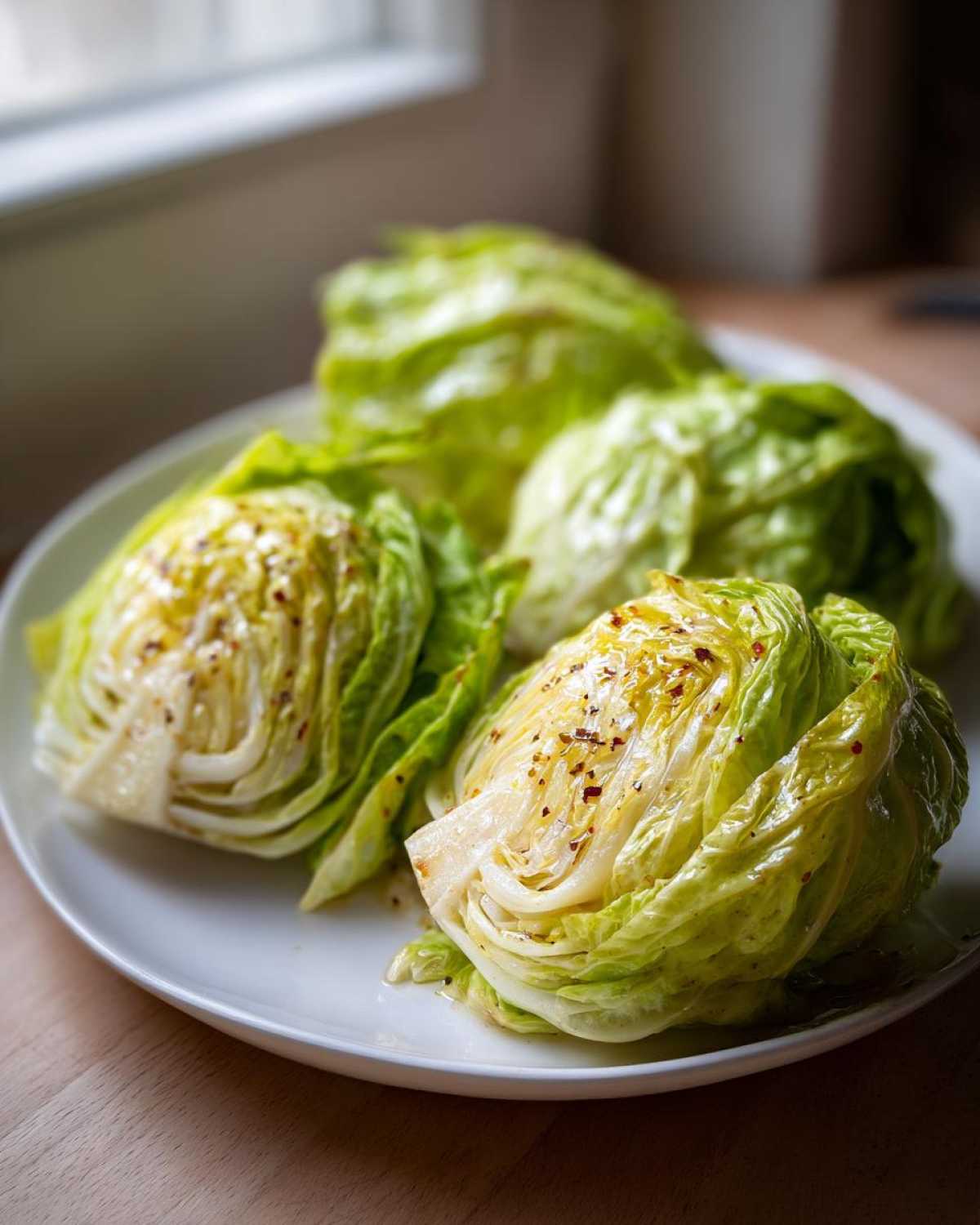 Four wedges of Roasted Cabbage with Garlic Butter served on a white plate, glistening with butter and spices.