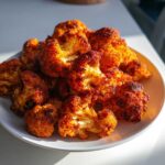 A plate piled high with beautifully caramelized Roasted Cauliflower with Smoked Paprika, showing crispy, orange-red edges.