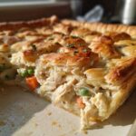 Close-up of a slice removed from a Sheet-Pan Chicken Potpie with Flaky Crust, showing creamy filling and golden pastry.