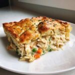 A thick slice of Sheet-Pan Chicken Potpie with Flaky Crust showing shredded chicken and vegetables in creamy sauce.