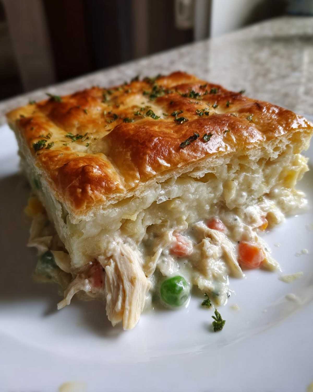 A close-up slice of Sheet-Pan Chicken Potpie with Flaky Crust showing shredded chicken, peas, and carrots in a creamy sauce.