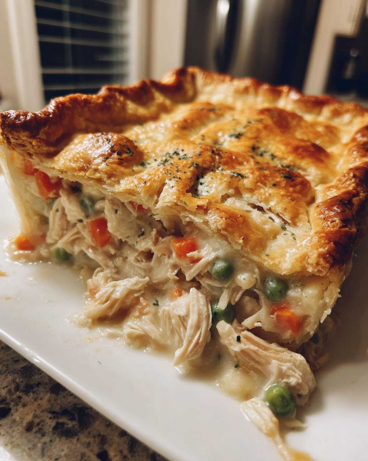 A close-up slice of Sheet-Pan Chicken Potpie showing shredded chicken, peas, carrots, and creamy filling under a golden flaky crust.