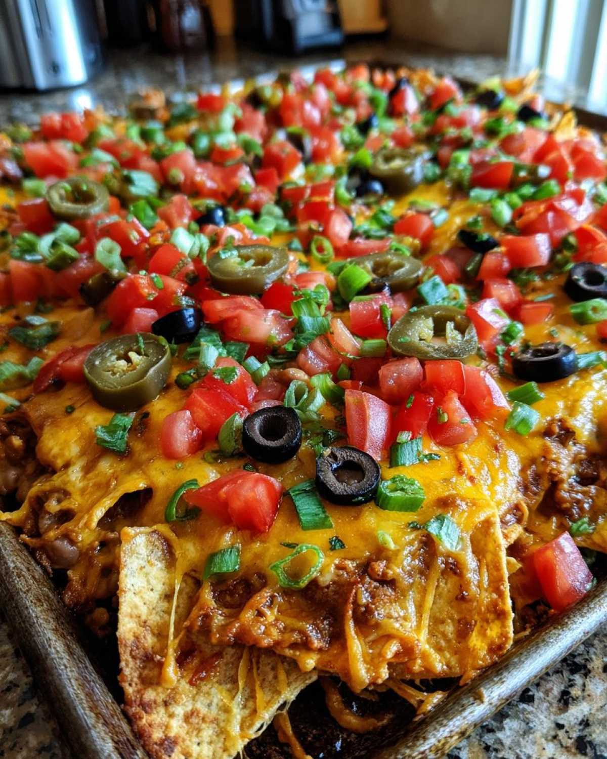 Close-up of fully loaded Sheet Pan Nachos with Refried Beans, topped with melted cheese, tomatoes, olives, and jalapeños.