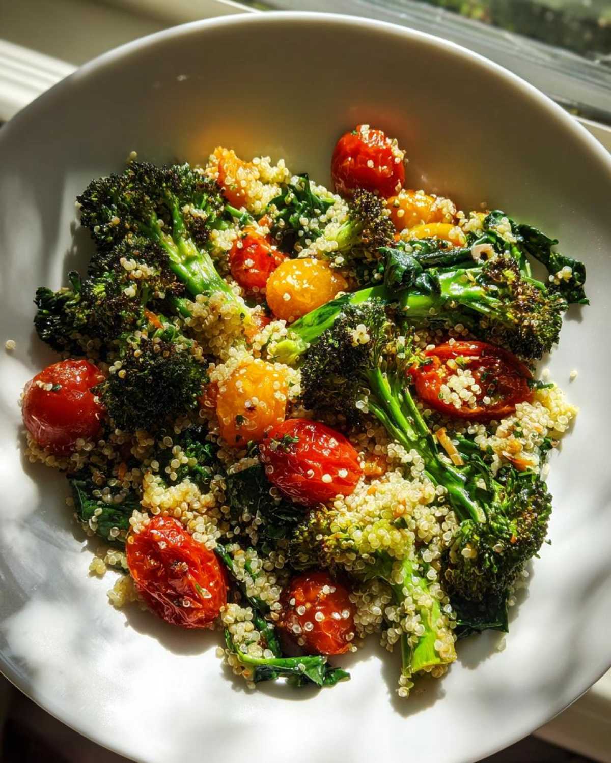A white bowl filled with Sheet Pan Salad with Toasted Veggies, featuring toasted broccoli, cherry tomatoes, and quinoa.