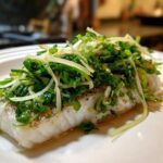 A perfectly cooked fillet of sea bass topped generously with vibrant green scallion sauce, ready to serve.