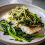 Close-up of a perfectly cooked fillet of sea bass topped with sizzling scallion sauce and served over green vegetables.