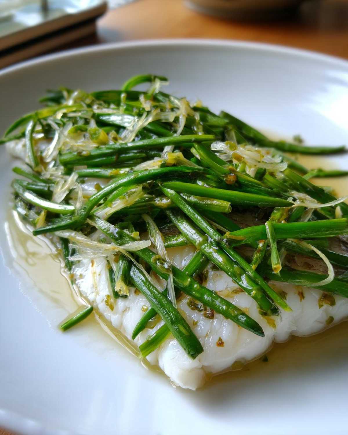 Close-up of a flaky white sea bass fillet topped generously with bright green scallion threads and sizzling sauce.