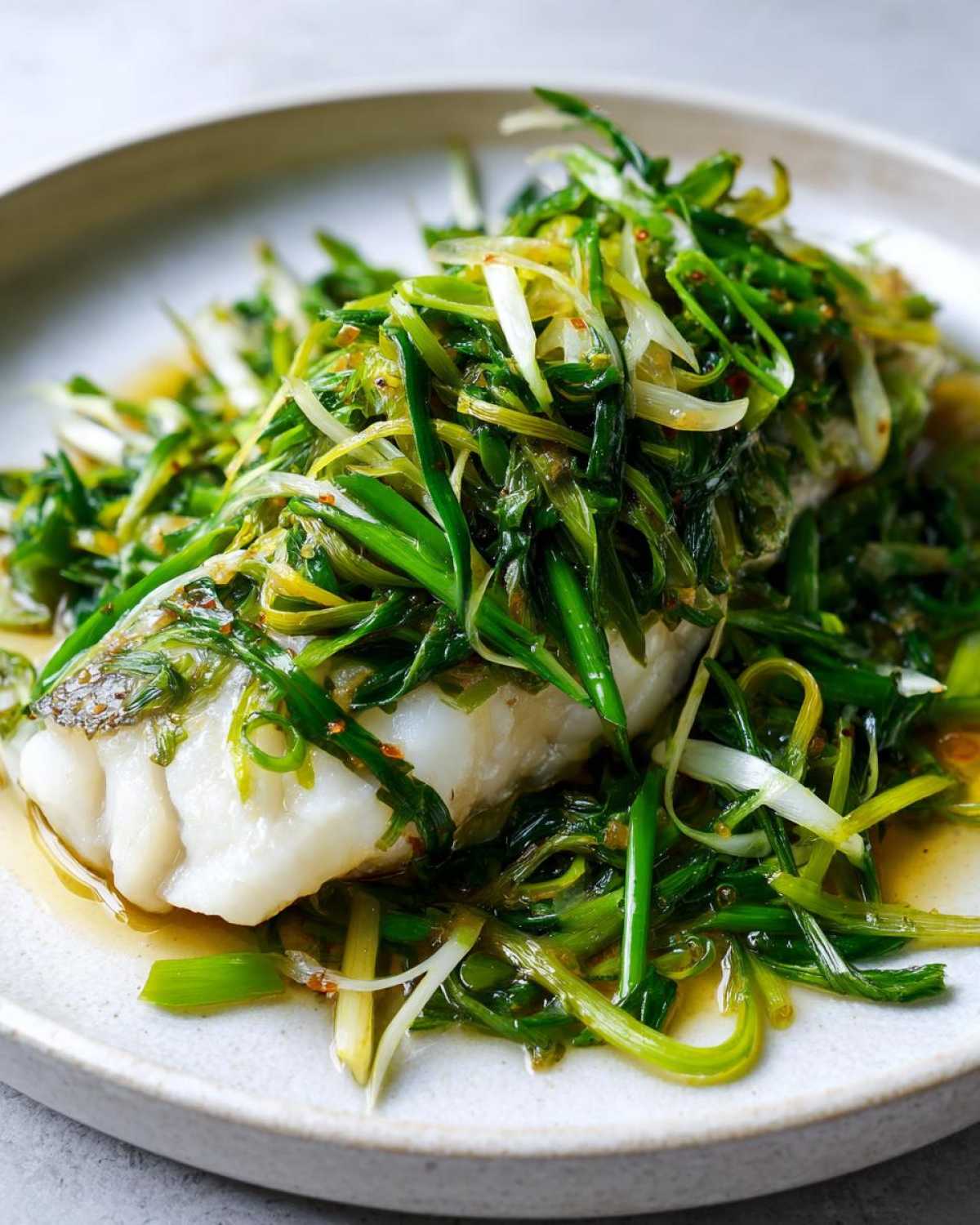 Close-up of a perfectly cooked sea bass fillet topped generously with bright green, sizzling scallion sauce.