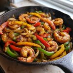 Close-up of seasoned shrimp mixed with colorful, sizzling peppers and onions in a black cast iron skillet, perfect for Shrimp Fajitas.