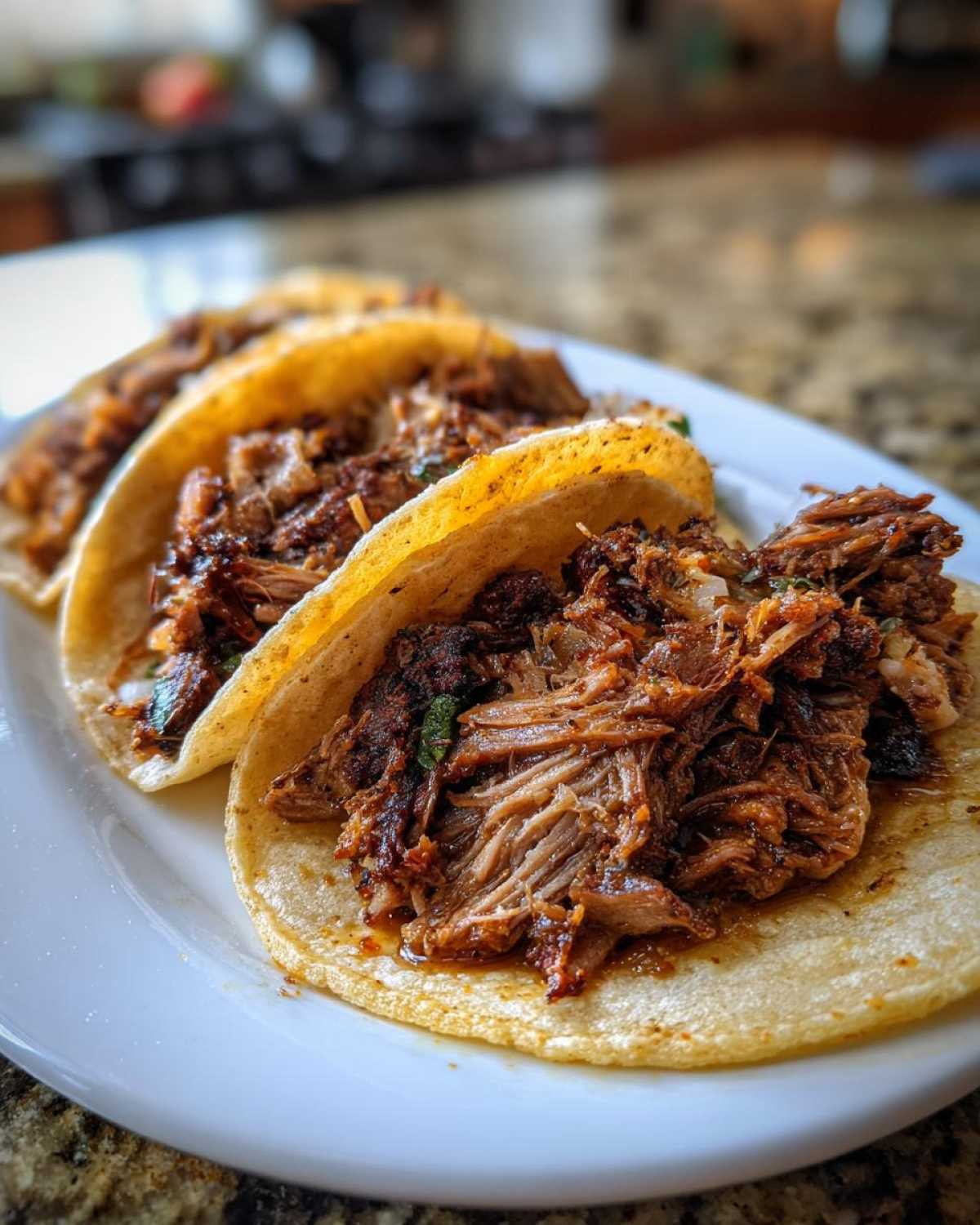 A close-up of three soft corn tortillas filled generously with shredded Slow-Cooked Pork Carnitas Tacos.