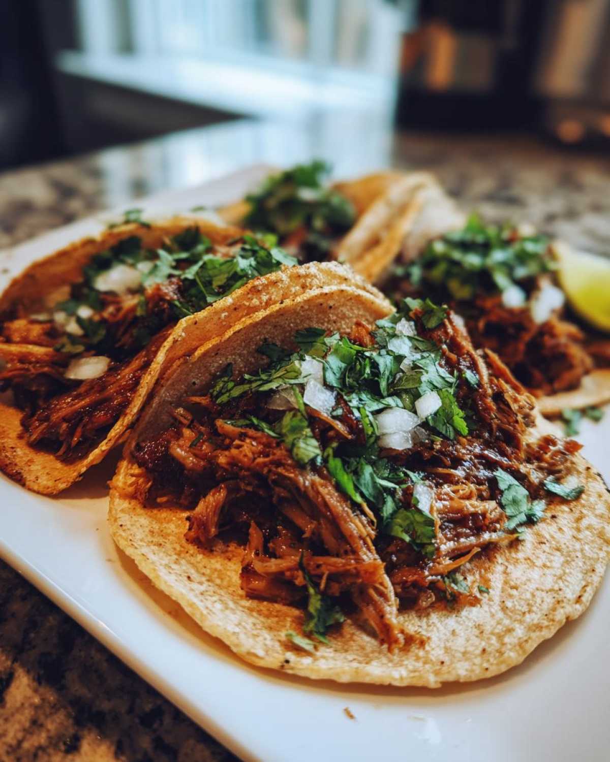 Close-up of several delicious Slow-Cooked Pork Carnitas Tacos topped with cilantro and diced white onion.