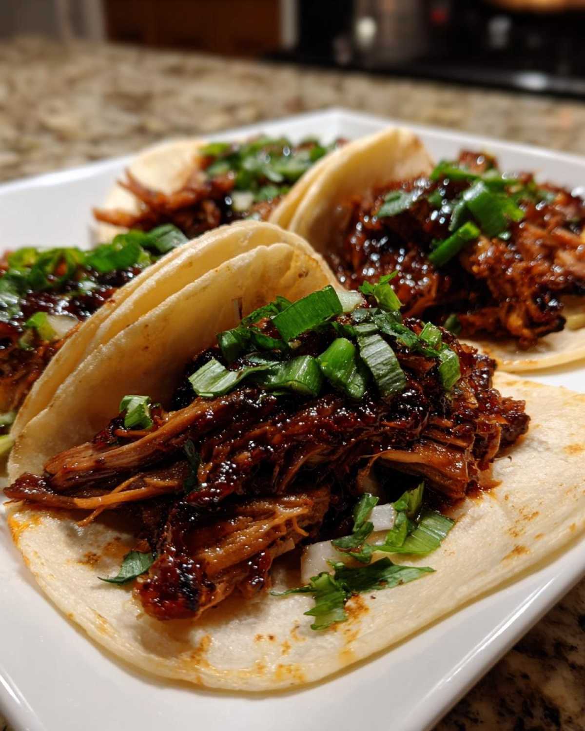 Four delicious Slow-Cooked Pork Carnitas Tacos filled with dark, saucy shredded pork and topped with green onions.