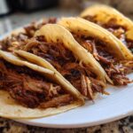 Close-up of four soft corn tortillas filled generously with shredded Slow-Cooked Pork Carnitas Tacos.