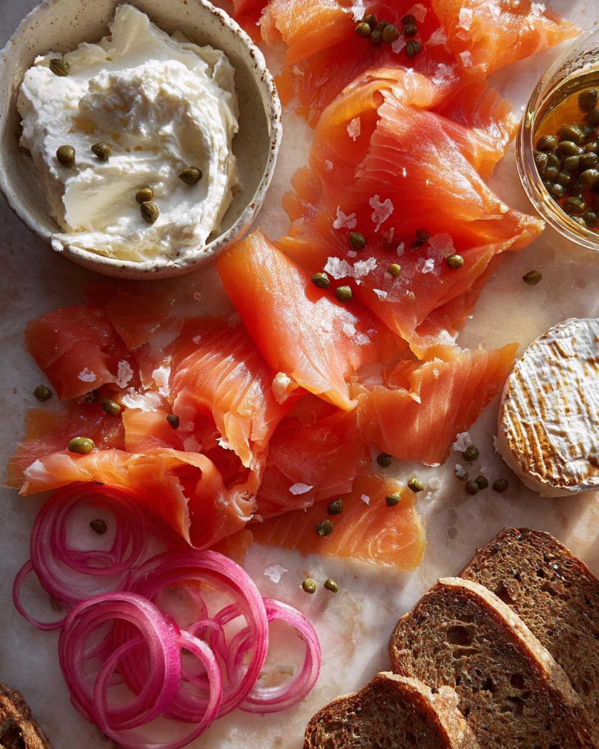 Close-up of smoked salmon slices, cream cheese, capers, red onion, and dark bread for a Breakfast Grazing Board with Smoked Salmon.