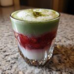 A layered Strawberry Cloud Matcha with Cold Foam drink showing white milk, red strawberries, green matcha, and white foam topping.