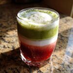 Close-up of a layered Strawberry Cloud Matcha with Cold Foam drink showing red, white, and green layers in a glass.
