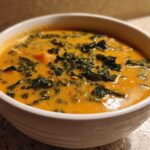 Close-up of a white bowl filled with creamy orange Sweet Potato Chowder with Kale.