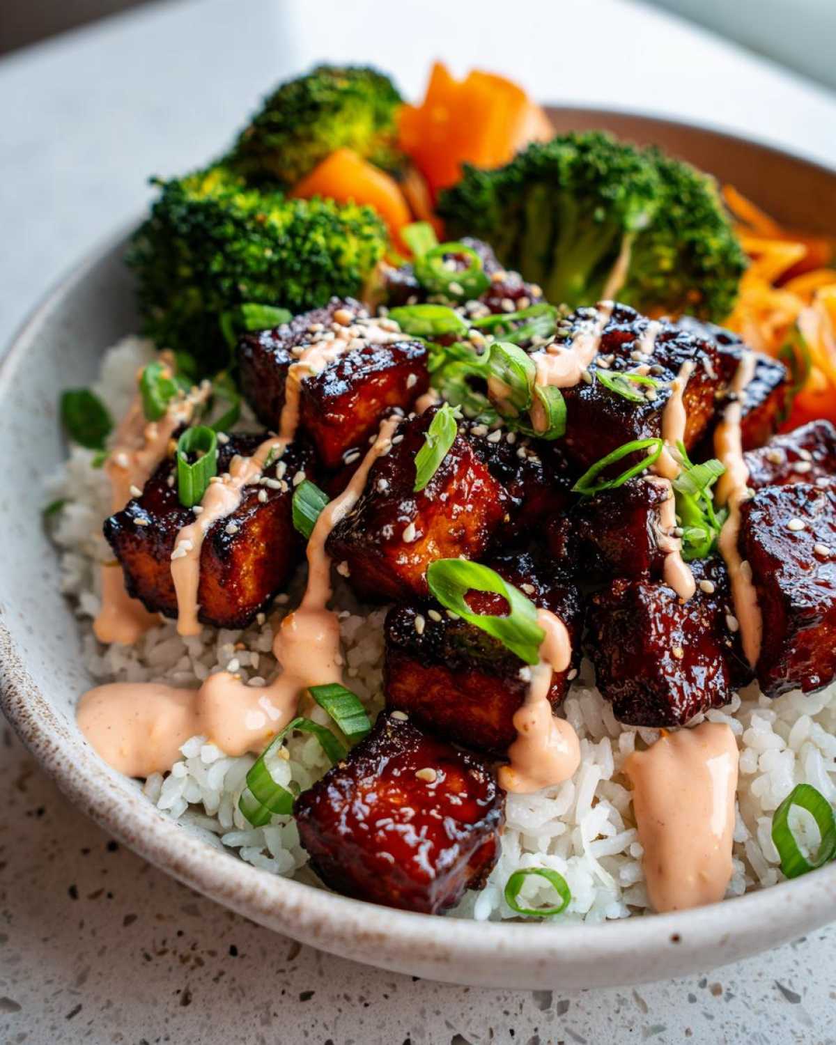 Close-up of a bowl featuring sticky Teriyaki Tofu Bowls with Kimchi Mayo drizzled over rice, broccoli, and carrots.
