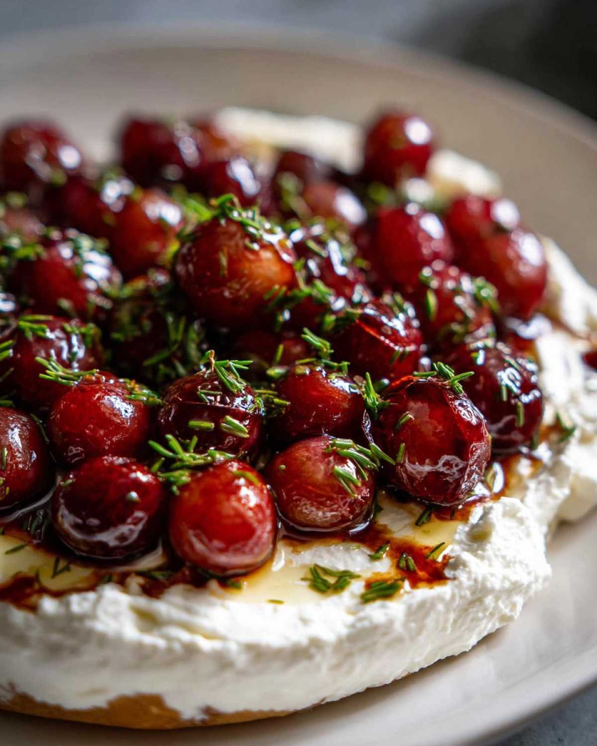 Close-up of Whipped Feta Dip with Roasted Grapes, topped with glossy, caramelized grapes and fresh herbs.