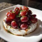 A serving of Whipped Feta Dip with Roasted Grapes topped with herbs in a white square bowl.