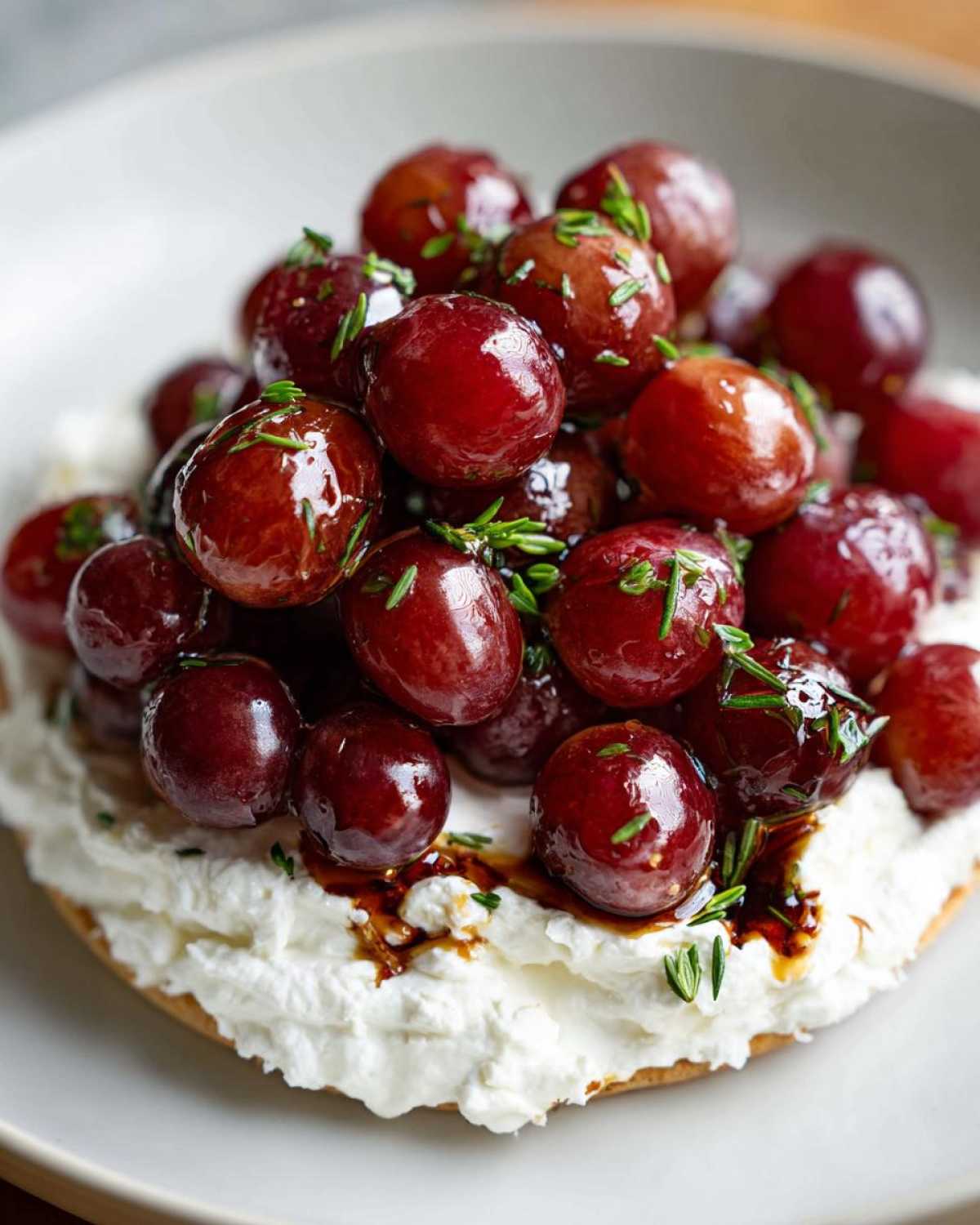 Close-up of Whipped Feta Dip with Roasted Grapes topped with herbs and balsamic glaze.