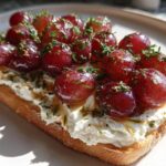 Close-up of Whipped Feta Dip with Roasted Grapes served on toasted bread, garnished with herbs.